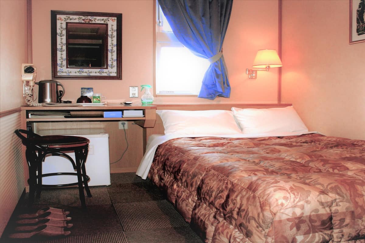 Une chambre d’hôtel avec un lit, un bureau, une chaise et une fenêtre avec des rideaux.