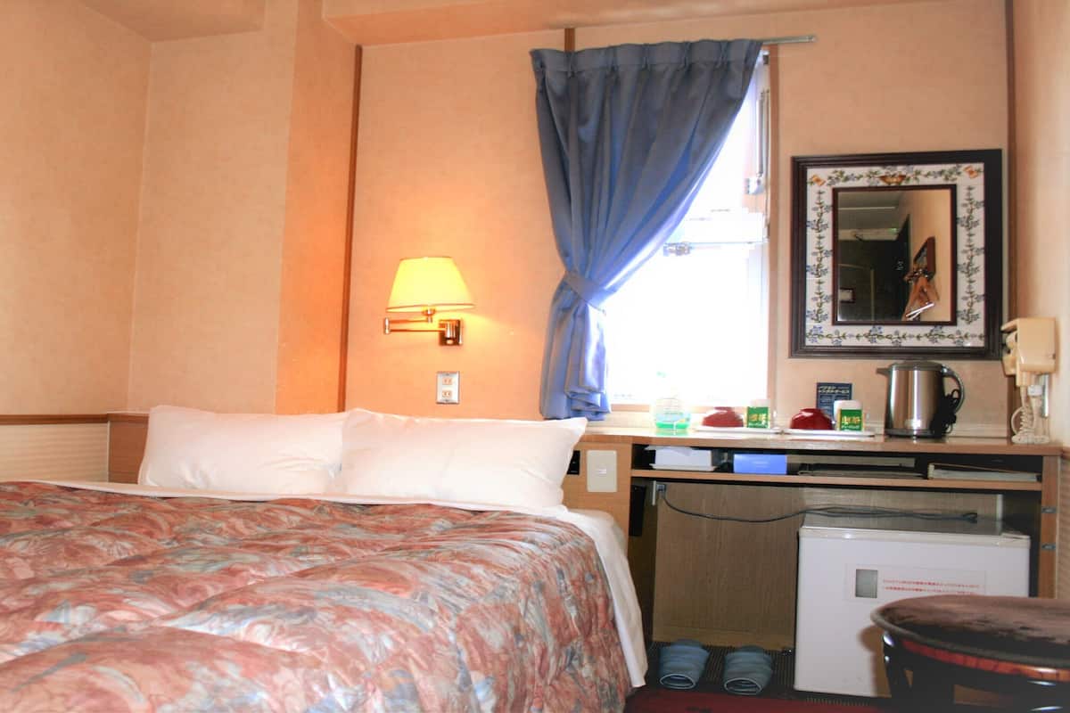 Une chambre d’hôtel comprenant un lit, un bureau avec une lampe, un miroir et une kitchenette.