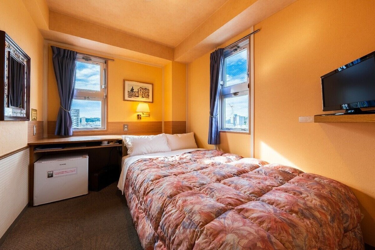 Hotellihuone, jossa on sänky, työpöytä, televisio ja ikkuna, jossa on verhot.