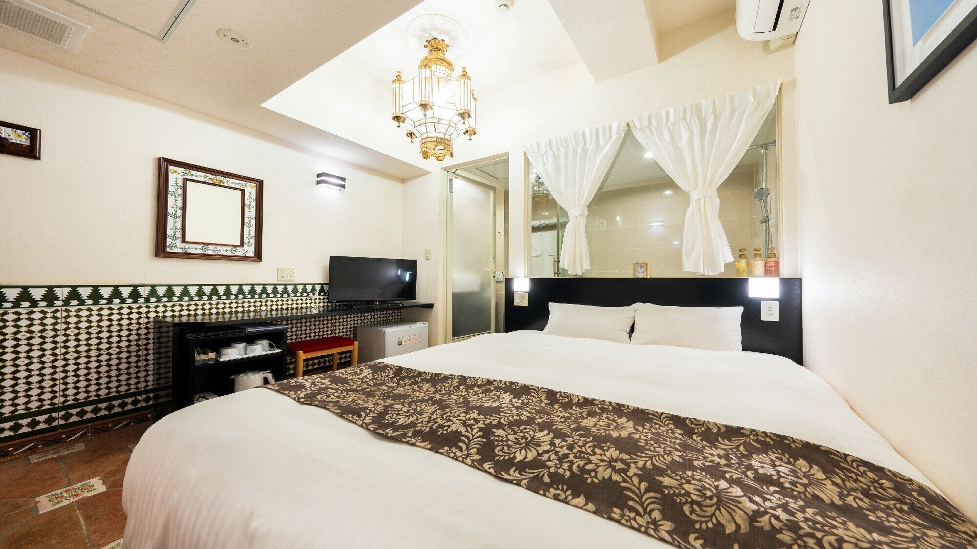 Quarto de hotel com cama, televisão, espelho e lustre.