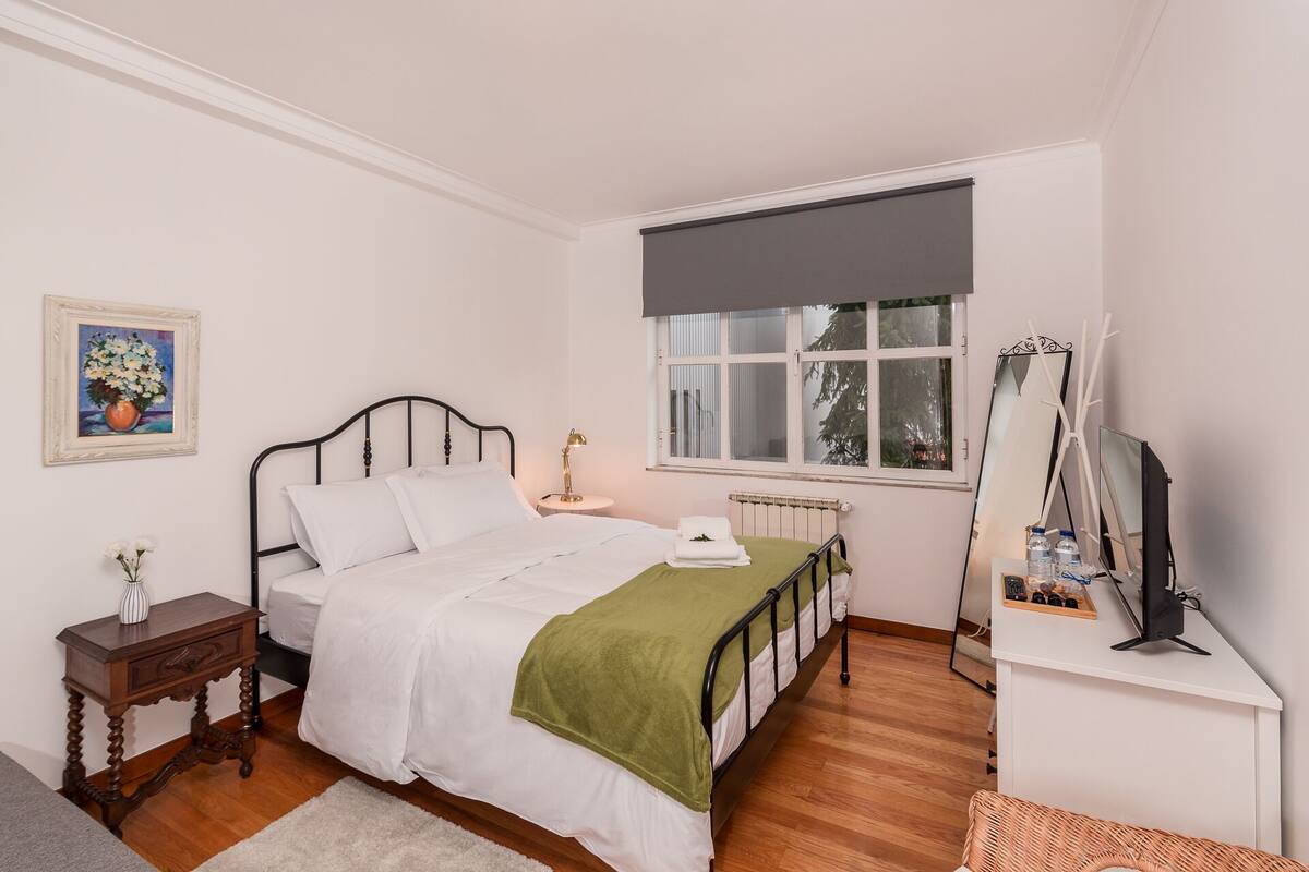 Une chambre à coucher comprenant un lit, une table de chevet, une lampe, une fenêtre, un radiateur et un miroir.