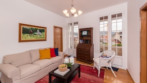 A living room with a beige sofa, a red rug, a wooden cabinet, and a white chair. - Fonte Branca Guest House (Braga)