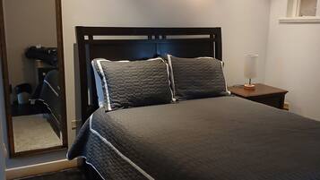 A bedroom with a bed, a nightstand, an air conditioning unit, a mirror, and a door.