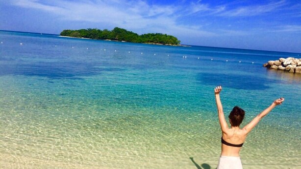 A beach with clear turquoise water, a person standing with arms raised, and a rocky outcrop in the distance. - Ocean View Condo....IN NEGRIL (NEGRIL)