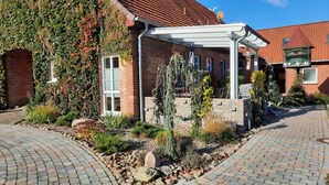 Une maison en briques avec un porche abrité, un jardin avec différentes espèces de plantes et une allée pavée.