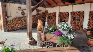 Un espace extérieur rustique agrémenté d’une pile de bois de chauffage, d’une charrette en bois décorée de fleurs et d’une lanterne.