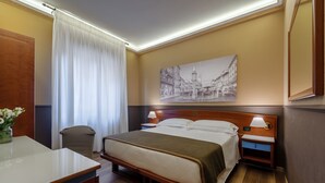 A hotel room with a bed, bedside tables, a desk, a chair, a large window with curtains, and a wall-mounted painting. - Mastino Rooms (Verona)