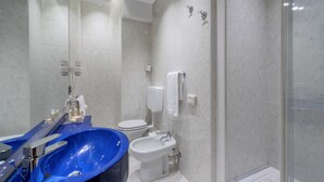 A modern bathroom with a blue bathtub, a white toilet, and a glass-enclosed shower area. - Mastino Rooms (Verona)