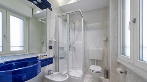 A modern bathroom with a glass-enclosed shower, a white toilet, and a blue sink. - Mastino Rooms (Verona)