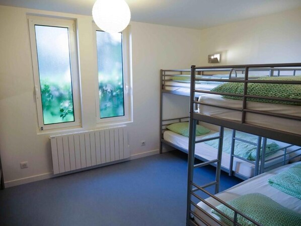 A room with bunk beds, a radiator, and two windows with a view of greenery. - Surf Camp XXIX (Saint-Jean-Trolimon)