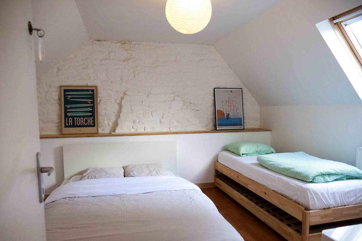 A bedroom with two beds, a sloped ceiling, and a white brick wall.