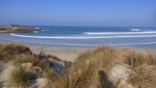 Une plage avec un ciel dégagé, des vagues et des dunes.