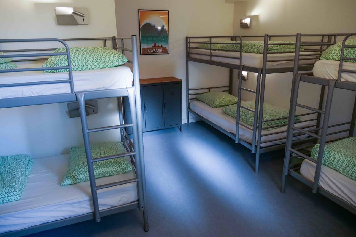 A dormitory room with bunk beds, a small cabinet, and a poster on the wall.