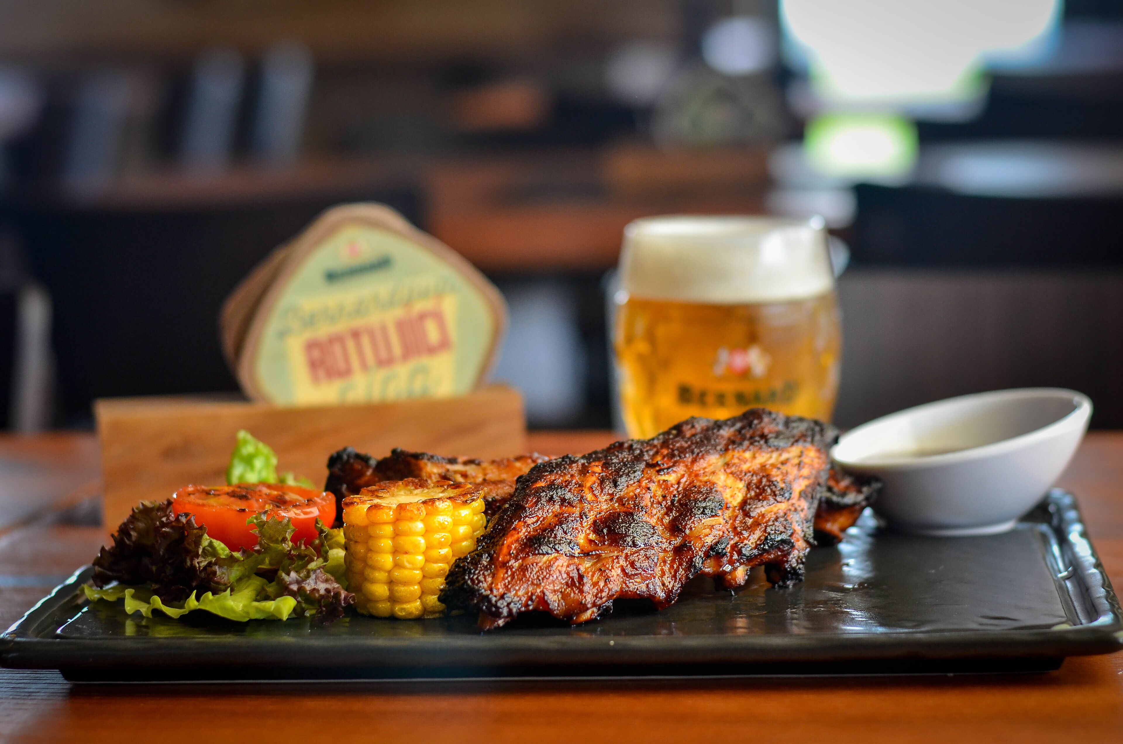 A plate of grilled meat with vegetables and a beer mug on a tray.