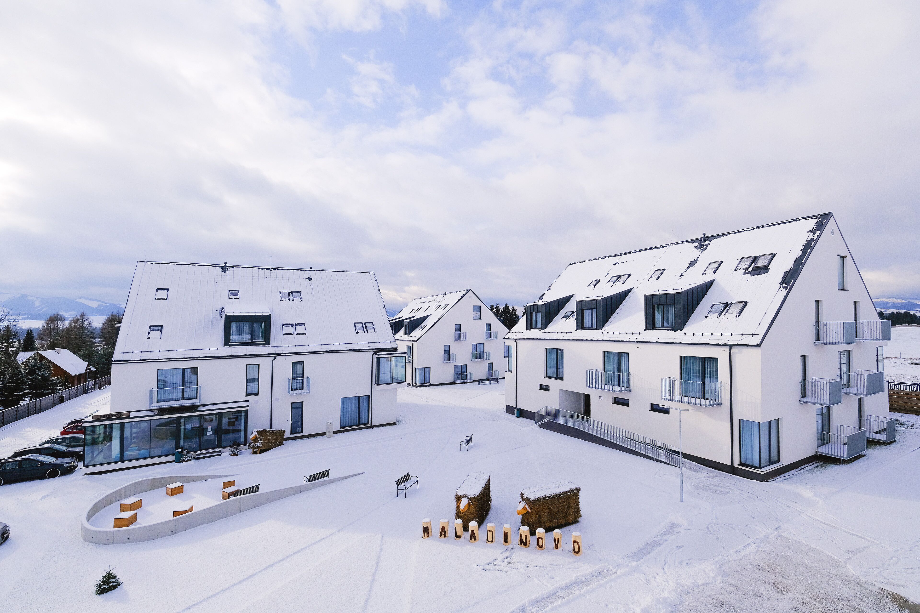 Un complejo moderno de edificios con varias estructuras blancas, ventanas amplias y suelo cubierto de nieve.