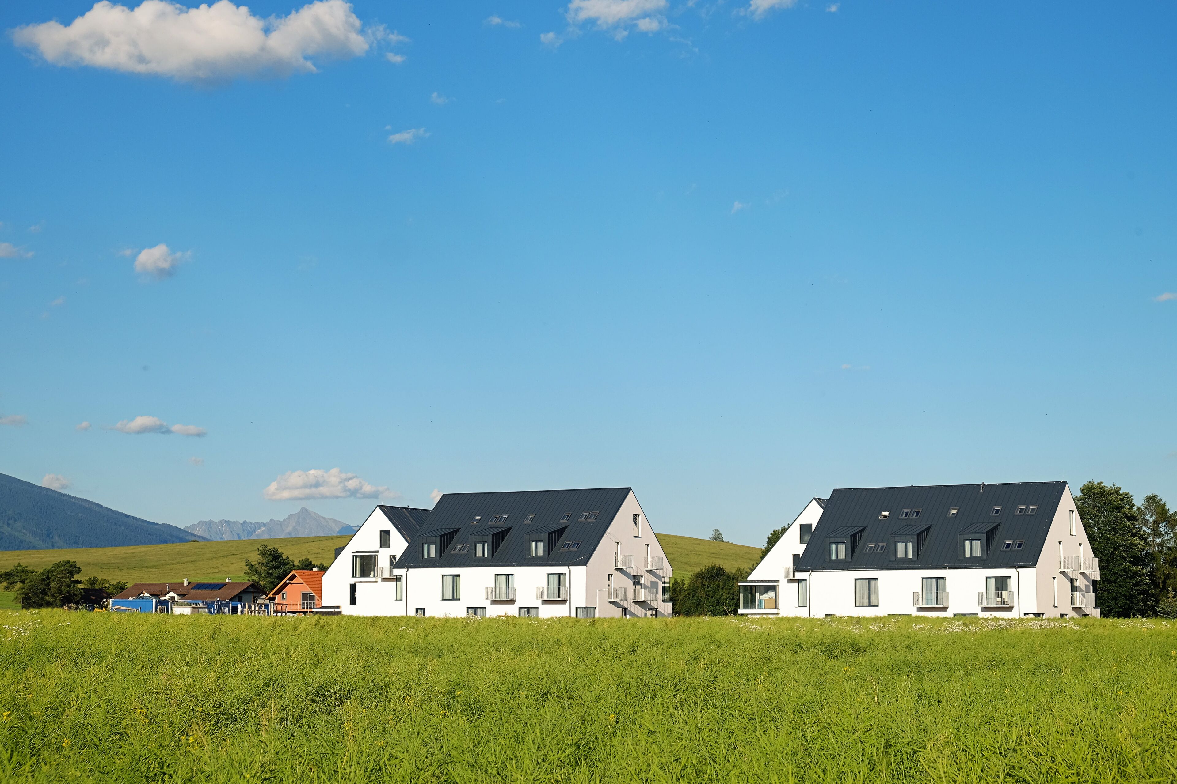 Una hilera de casas modernas con techos inclinados y amplias ventanas, con un cielo azul despejado y colinas verdes de fondo.