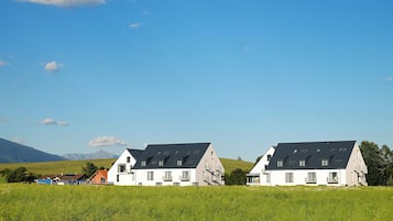 Une rangée de maisons modernes, dotées de toits inclinés et de nombreuses fenêtres, se dressant sur un fond de ciel bleu clair et de collines verdoyantes.