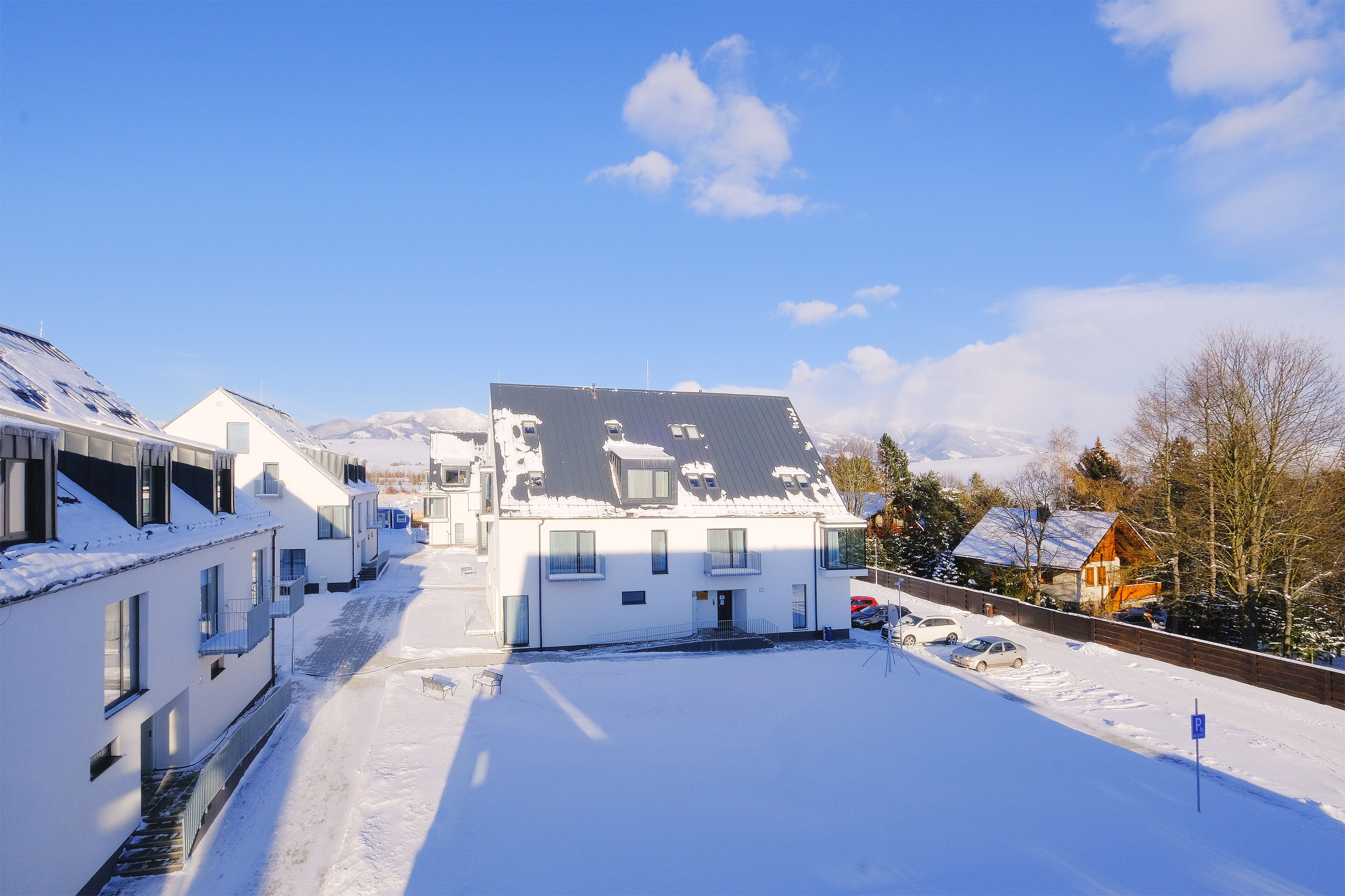 Una zona residencial cubierta de nieve con casas modernas, un área de estacionamiento y una montaña al fondo.