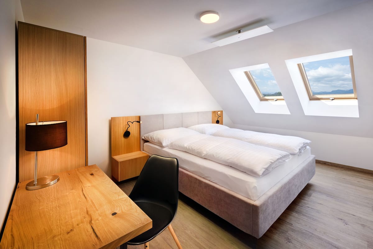 A modern bedroom with a bed, a desk, a chair, and two skylights.