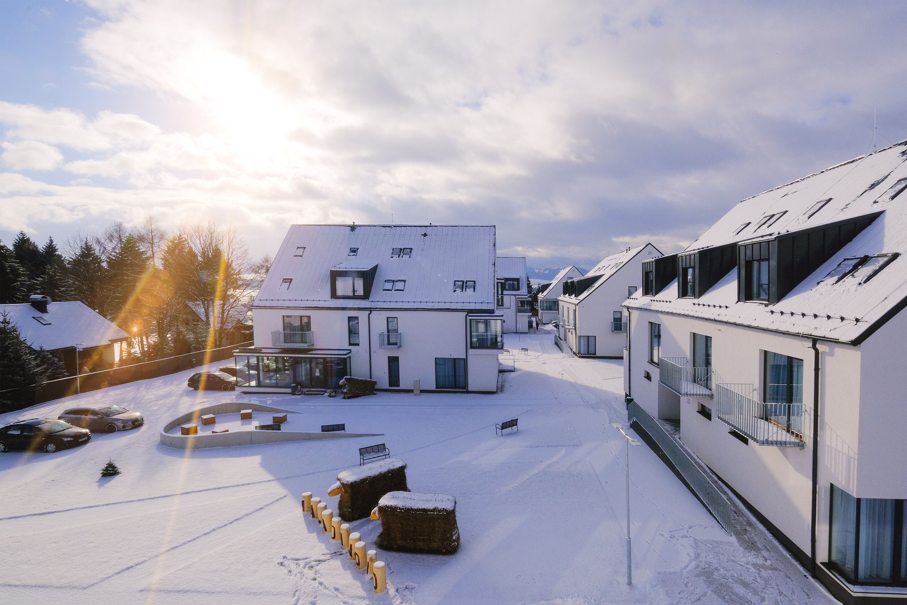 A modern building with a flat roof and large windows, surrounded by snow-covered ground and parked cars.