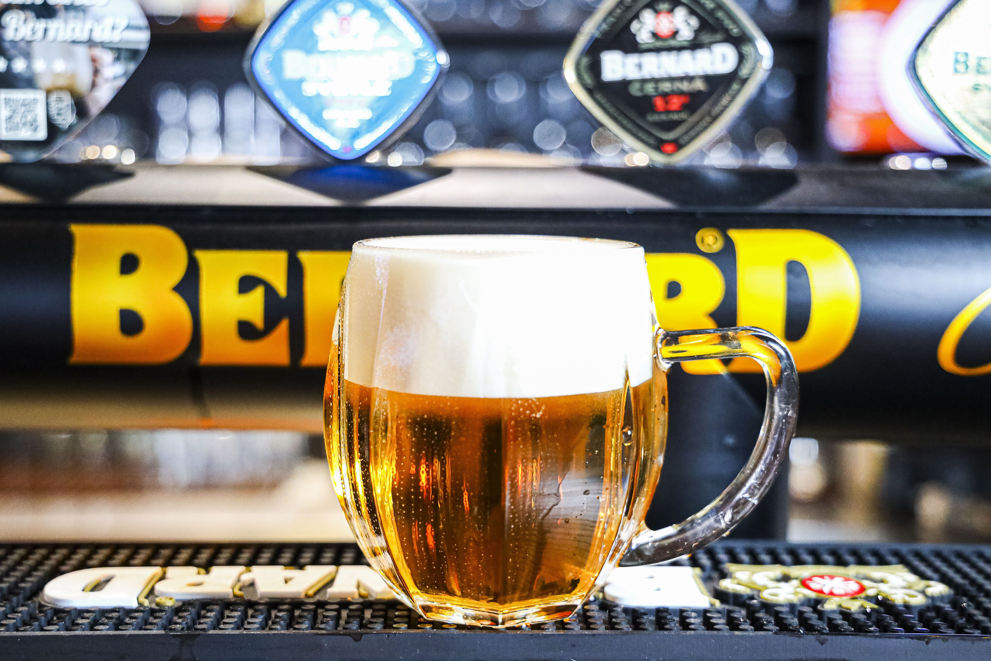 A glass of beer with a frothy head, placed on a bar counter with a beer tap labeled "BEERD" in the background.
