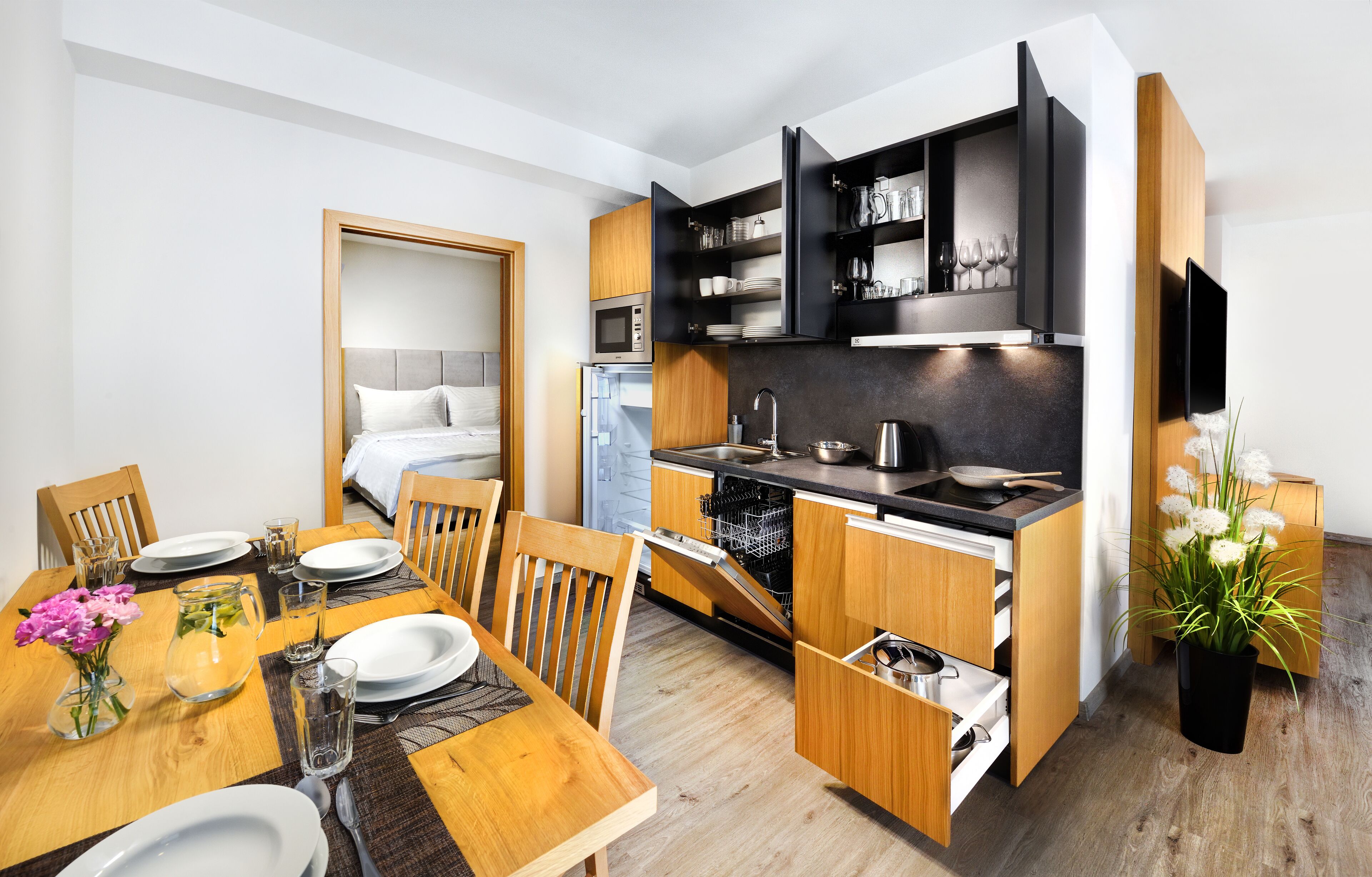 A compact kitchen with integrated appliances, a dining area with a wooden table and chairs, and a small refrigerator.