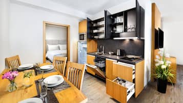 A compact kitchen with integrated appliances, a dining area with a wooden table and chairs, and a small refrigerator.