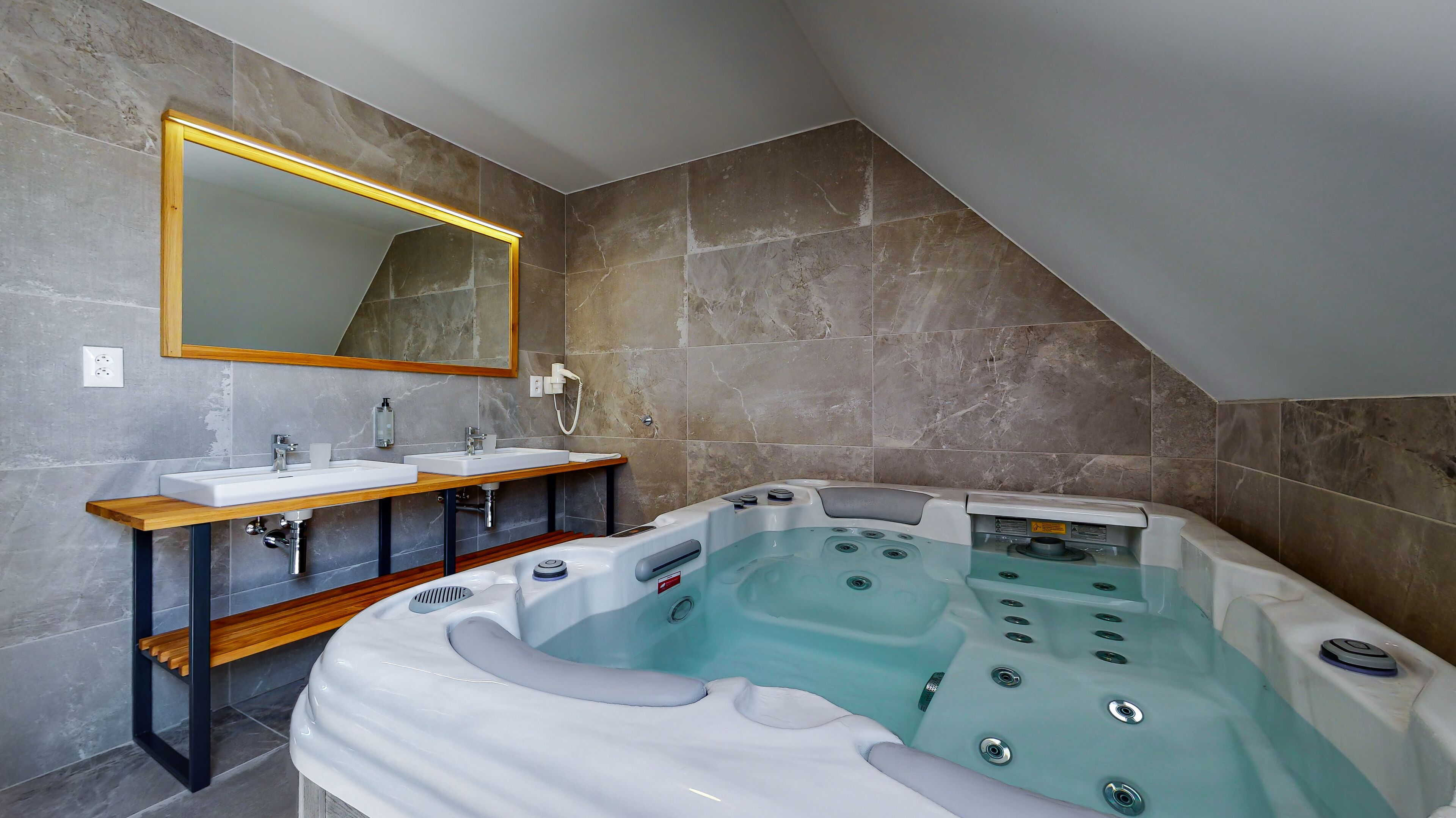 A modern bathroom with a large bathtub, two sinks, a wooden vanity, and a large mirror.