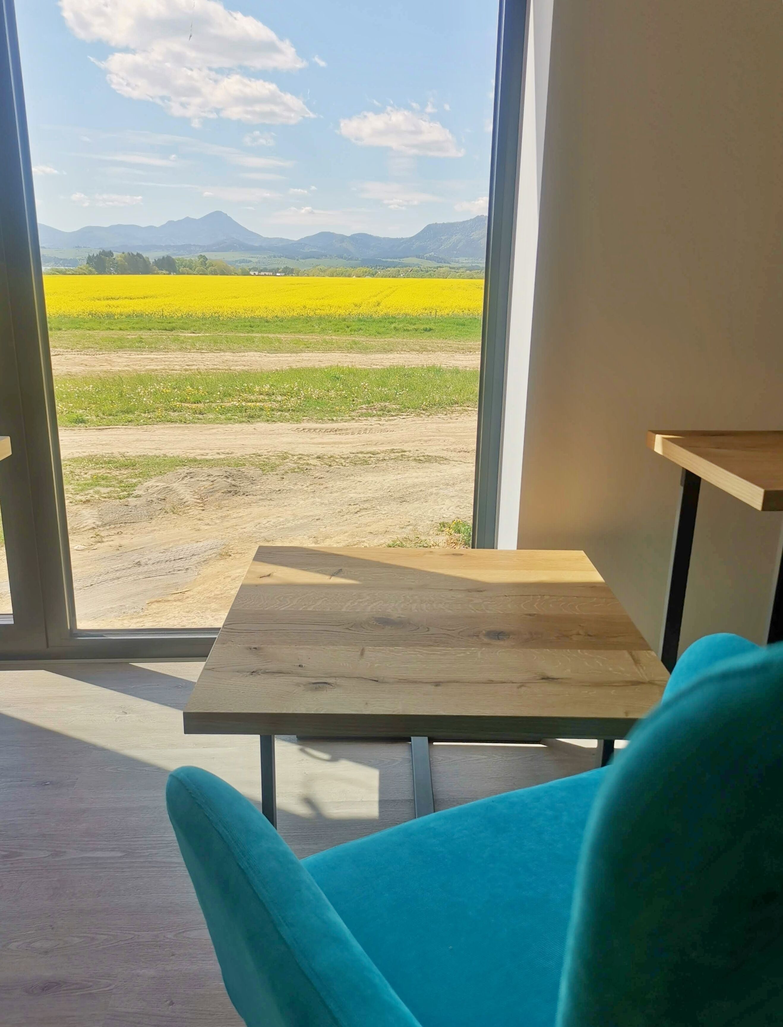 Una habitación con un ventanal que ofrece vistas a un campo amarillo y montañas lejanas.