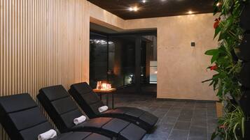 Un área de spa con sillones reclinables negros, una mesita con velas y una pared cubierta de plantas.