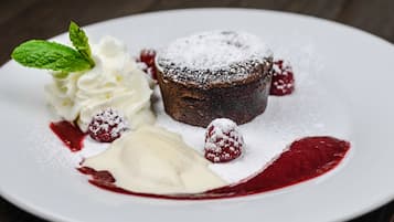 Un plato de postre con pastel de chocolate, crema batida, frambuesas y una hoja de menta.