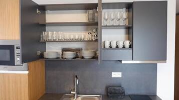 Cocina compacta con microondas integrado, pileta de acero inoxidable y estanterías abiertas con cristalería y vajilla.