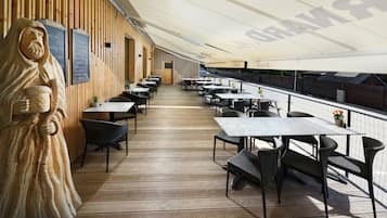 Ein Restaurant mit einer langen Holzterrasse, Tischen und Stühlen.