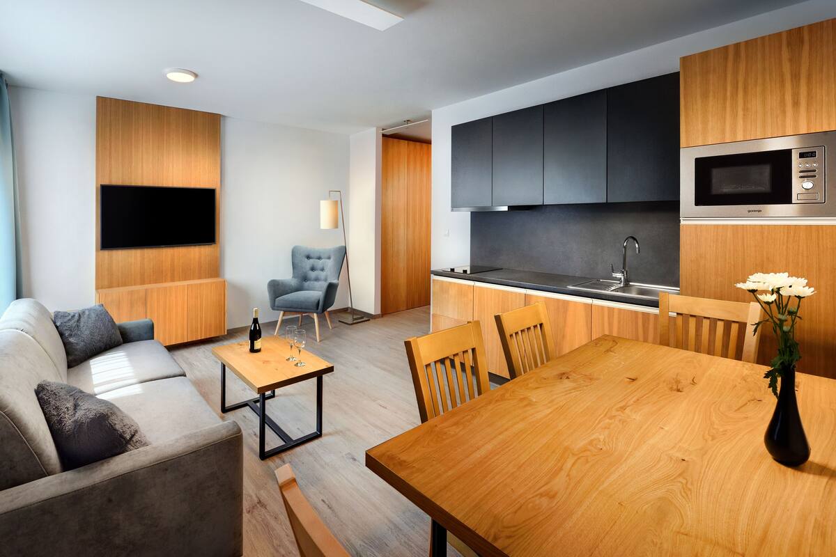 A modern living room with a sofa, a dining table, and a kitchen area with a microwave and cabinets.