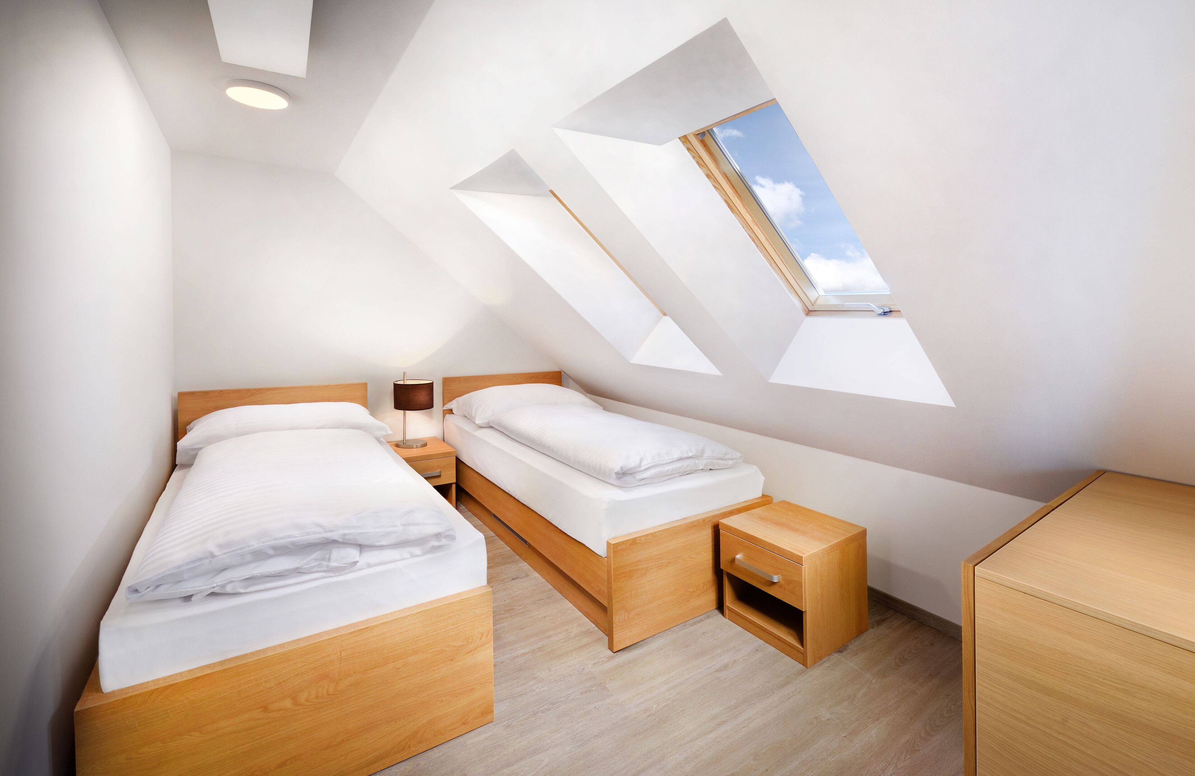 A modern bedroom with a sloped ceiling and skylight, wooden furniture, and a simple layout.