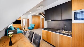 A modern kitchen with a black countertop and wooden cabinets, a dining area with a wooden table and chairs, and a living area with a blue sofa and a small coffee table.