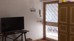 A room with a television on a wooden stand, a small stool, a waste bin, and a patterned glass door. - Villa Pomelia a stone's throw from the sea (Palermo)