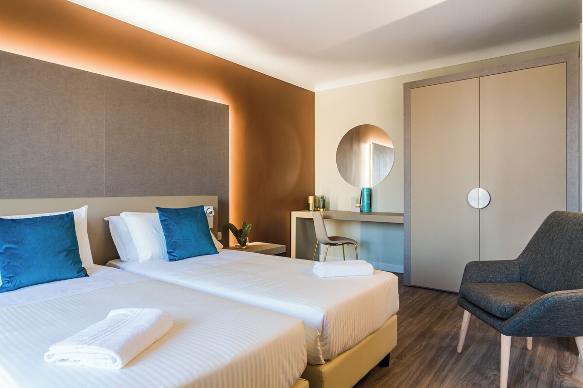 A hotel room with two beds, a desk, a chair, a mirror, and a wardrobe.
