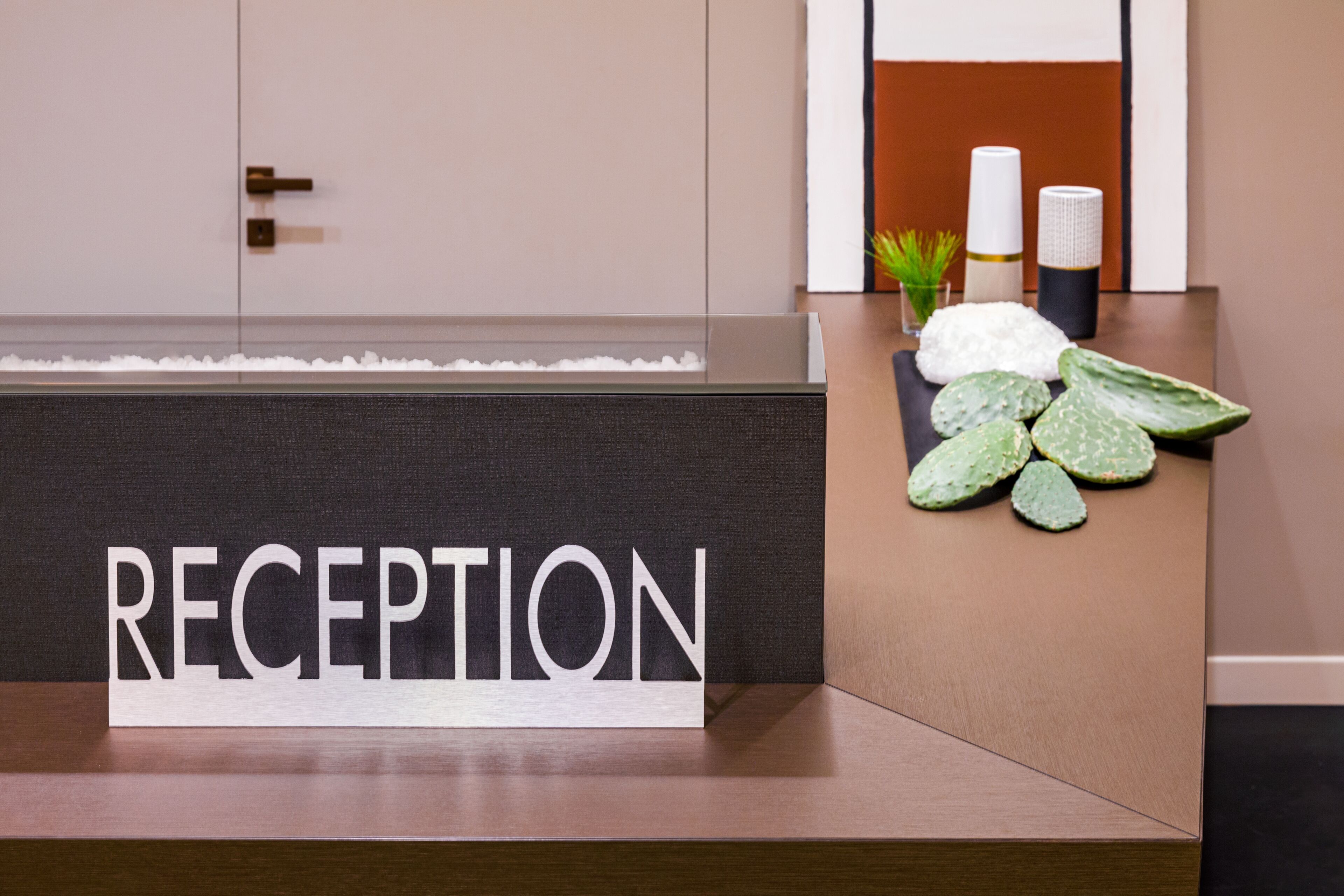 A reception desk with a sign that reads "RECEPTION" and a small plant on the counter.