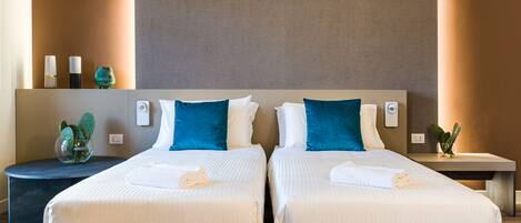 A hotel room with two beds, a bedside table, a nightstand, and a wall-mounted light fixture.
