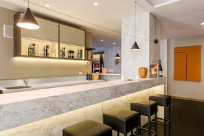 A modern bar area with a marble countertop, bar stools, and a large mirror above the counter.