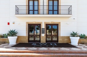 L'ingresso di un hotel con una porta doppia, un balcone con ringhiera e piante in vasi su entrambi i lati.