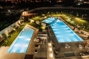 Una vista aerea di un hotel con due ampie piscine, aree relax all'aperto e curato giardino.