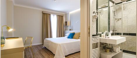 A hotel room with a bed, bedside table, lamp, and a view of the bathroom.