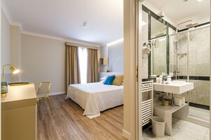 Una camera d'albergo con un letto, un comodino, una lampada e vista sul bagno.