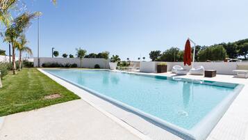 A rectangular swimming pool with a tiled edge, surrounded by a white deck and a low wall.