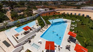 A large outdoor swimming pool with multiple sections, surrounded by lounge chairs and umbrellas.