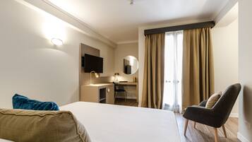 A hotel room with a large bed, a desk with a chair, a TV, a mirror, and a window with curtains.