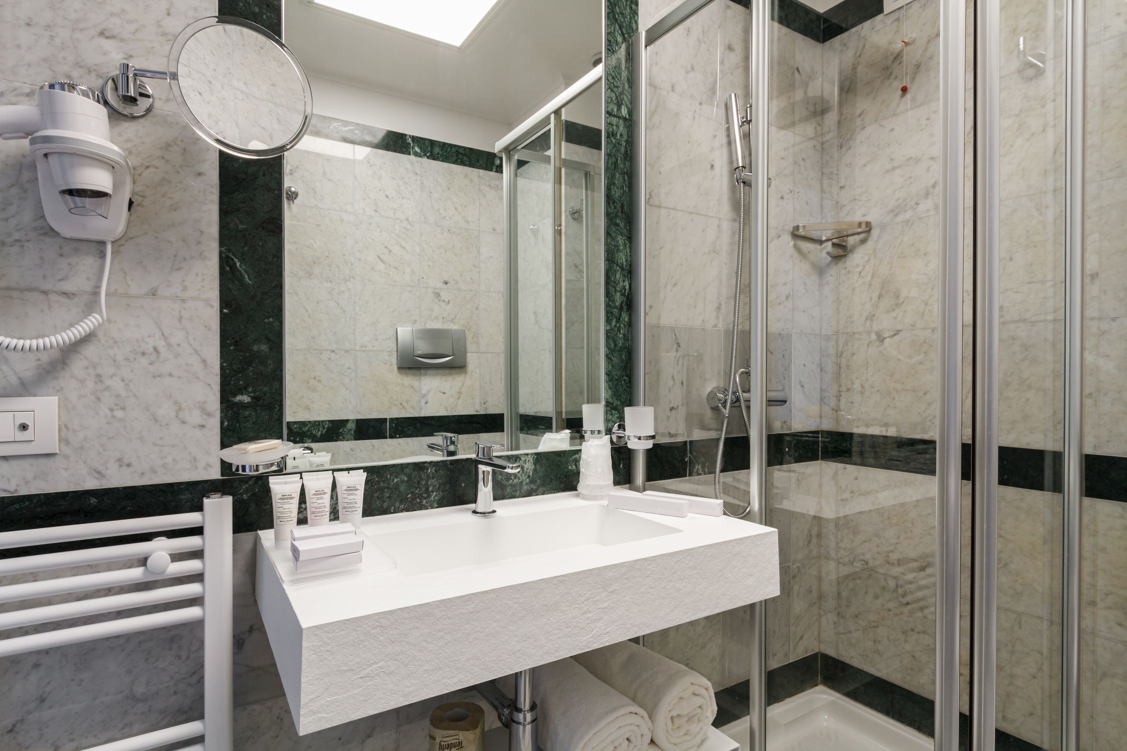 A modern bathroom with a white sink, a handheld mirror, a handheld hair dryer, and a glass-enclosed shower.