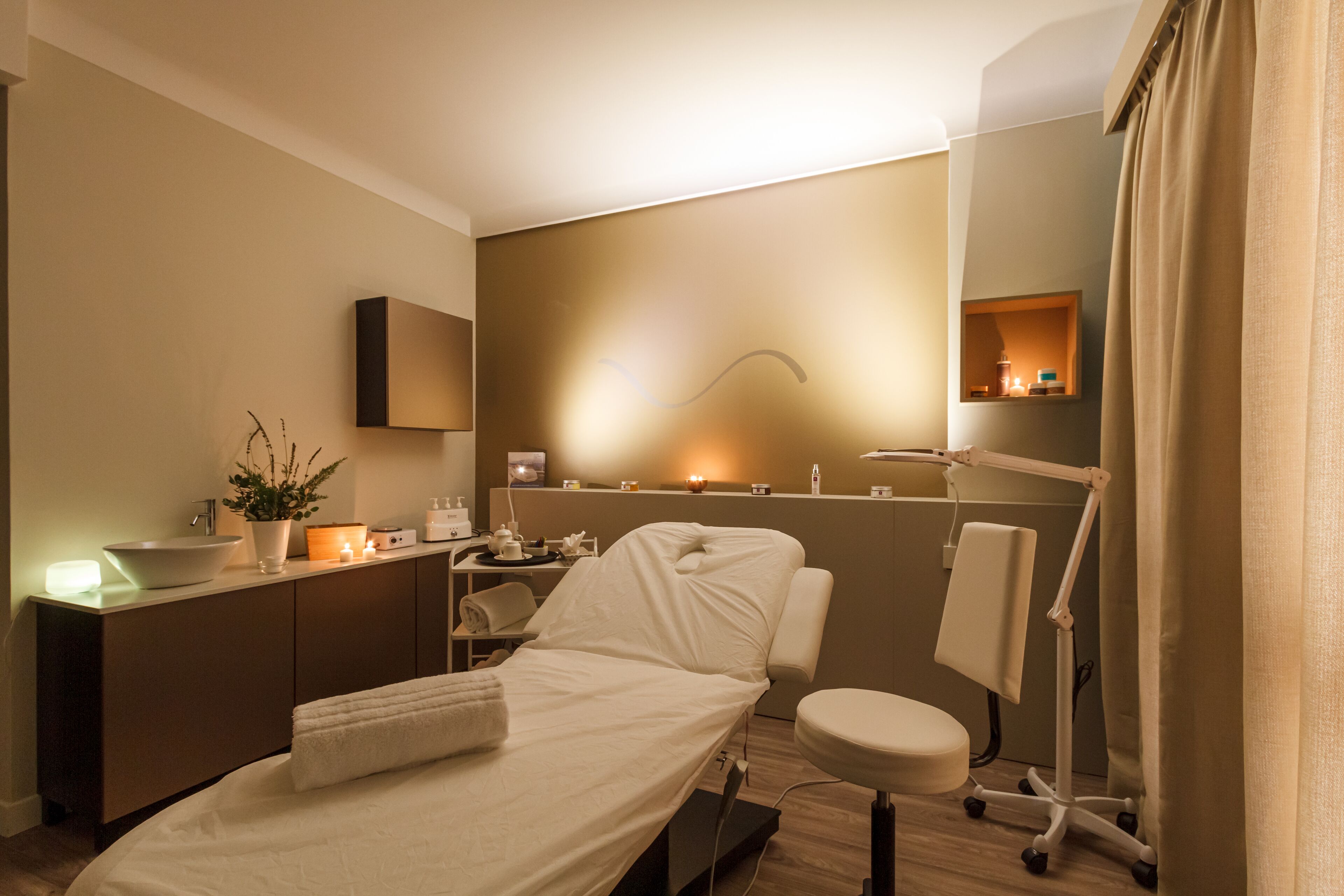 A modern hotel room with a bed, bedside table, and a small desk area with a plant and candles.